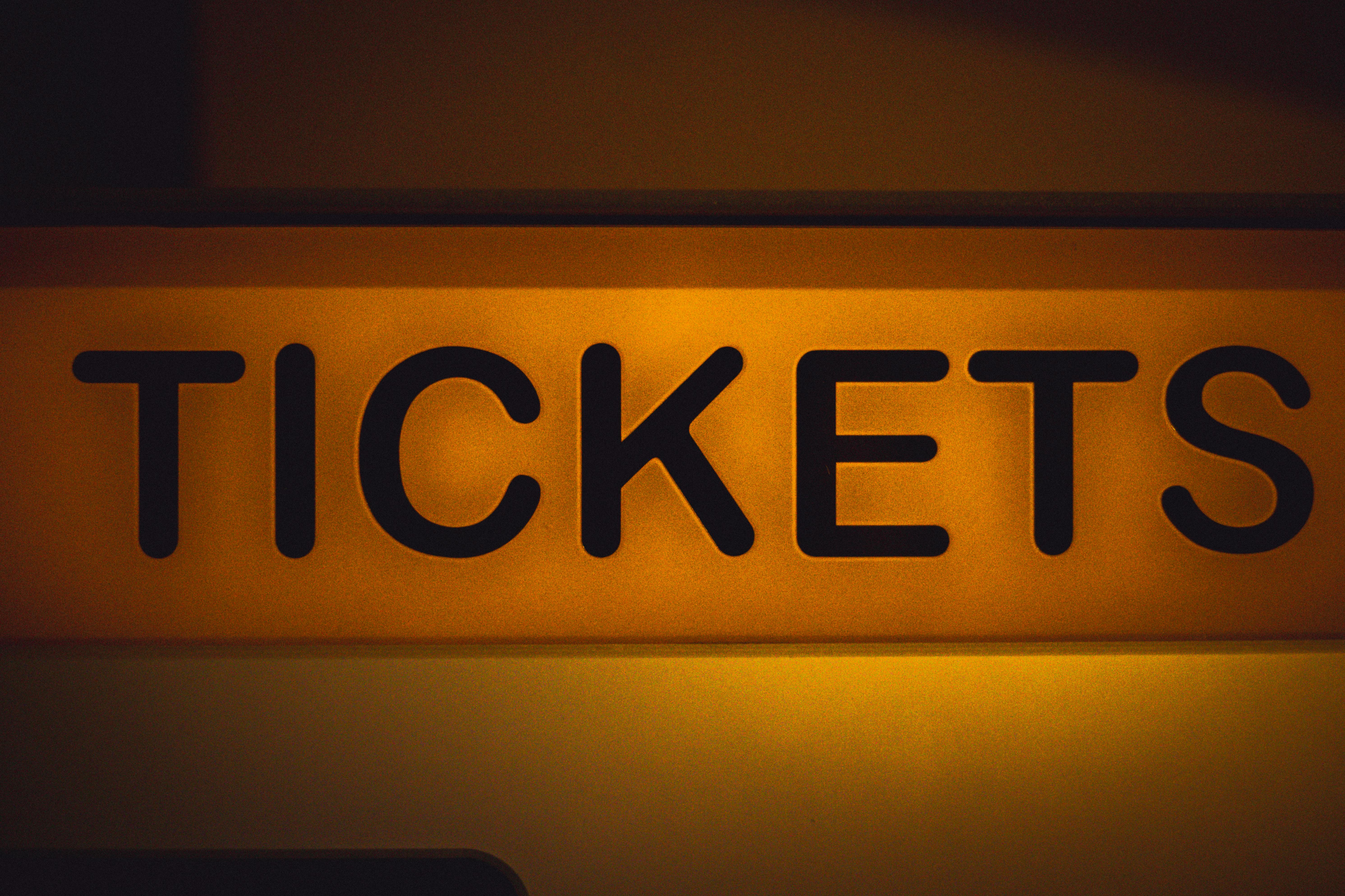 Close-up of an illuminated yellow ticket sign against a dark background.